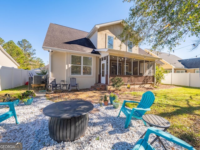 back of house featuring a lawn, a sunroom, a patio, and an outdoor fire pit