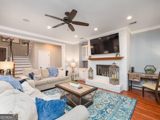 living room featuring dark hardwood / wood-style floors, ceiling fan, crown molding, and a brick fireplace