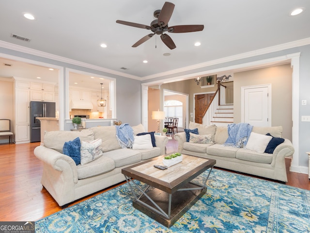 living room featuring ceiling fan, ornamental molding, and light wood-type flooring