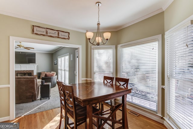 dining area featuring a fireplace, ceiling fan with notable chandelier, light hardwood / wood-style floors, and crown molding