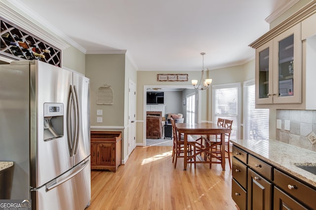 kitchen with stainless steel refrigerator with ice dispenser, light hardwood / wood-style flooring, ornamental molding, light stone countertops, and dark brown cabinetry