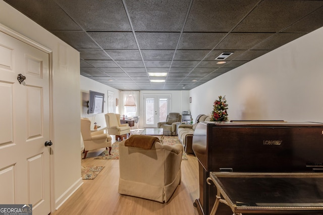 living room with light hardwood / wood-style flooring, a drop ceiling, and french doors