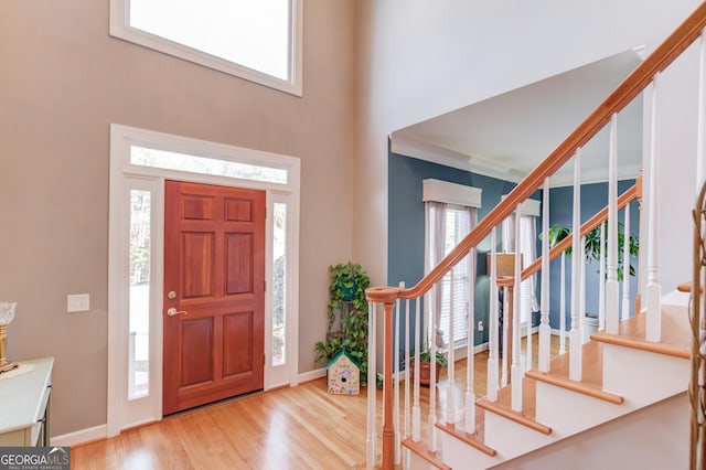 foyer entrance with a high ceiling, crown molding, a wealth of natural light, and light hardwood / wood-style flooring