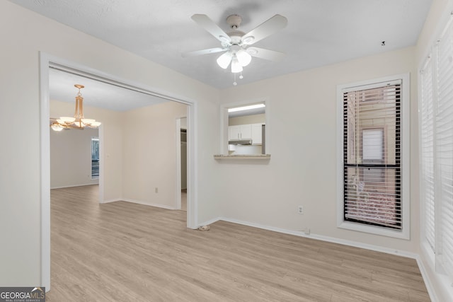 unfurnished room with ceiling fan with notable chandelier, a textured ceiling, and light wood-type flooring