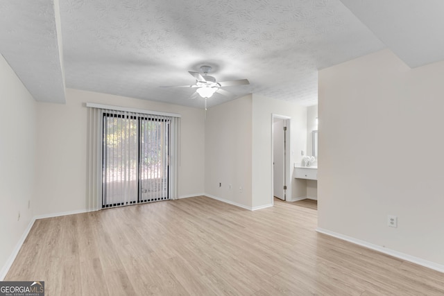 unfurnished room with ceiling fan, light wood-type flooring, and a textured ceiling