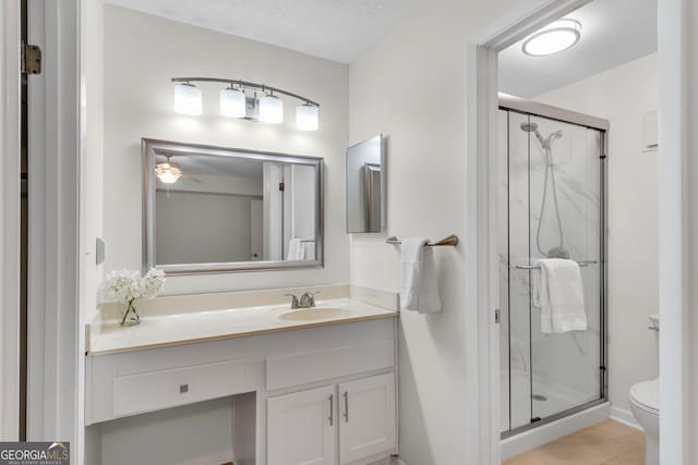 bathroom featuring vanity, a shower with door, tile patterned floors, ceiling fan, and toilet