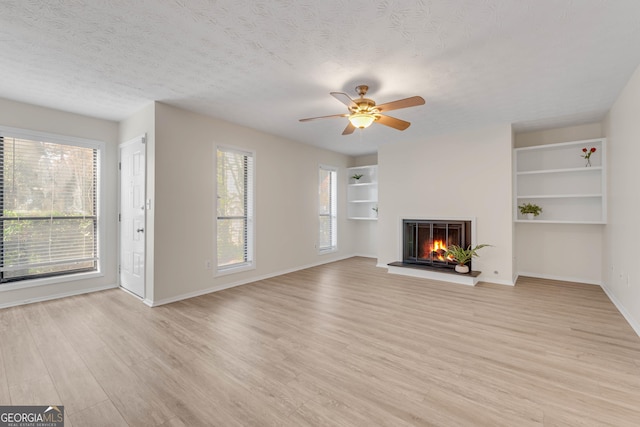 unfurnished living room with ceiling fan, light hardwood / wood-style flooring, a healthy amount of sunlight, and a textured ceiling