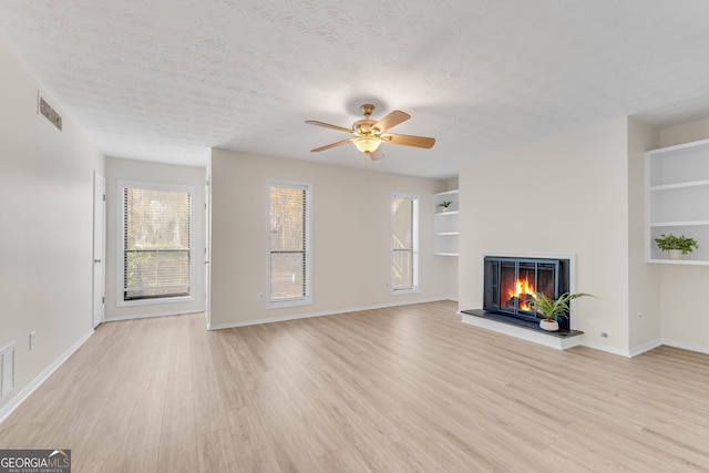 unfurnished living room featuring built in shelves, ceiling fan, light hardwood / wood-style flooring, and a textured ceiling