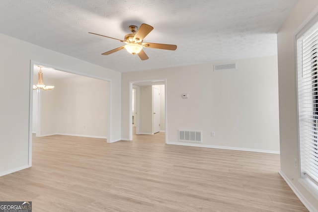 empty room with ceiling fan with notable chandelier, a textured ceiling, and light hardwood / wood-style flooring