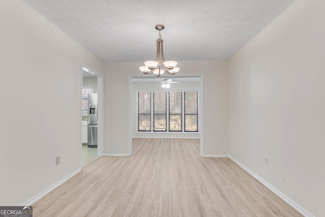 unfurnished dining area with ceiling fan with notable chandelier, a textured ceiling, and light hardwood / wood-style floors