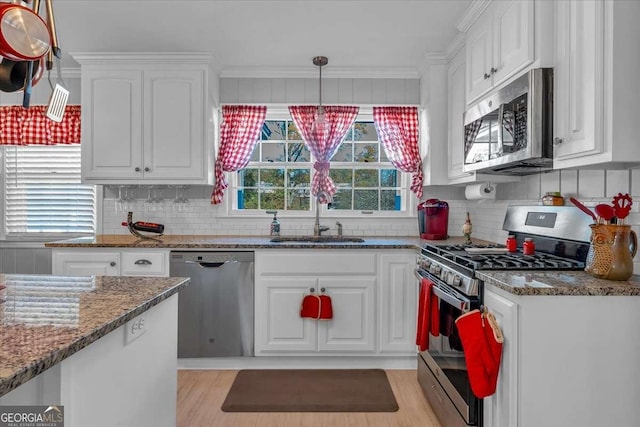 kitchen with stainless steel appliances, dark stone counters, sink, white cabinetry, and decorative light fixtures