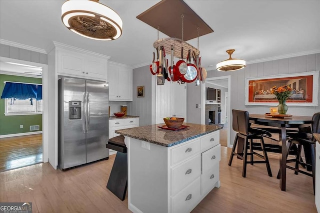 kitchen featuring a center island, stainless steel fridge with ice dispenser, white cabinetry, ornamental molding, and dark stone countertops