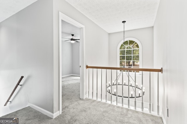 hall featuring a textured ceiling, carpet floors, and an inviting chandelier