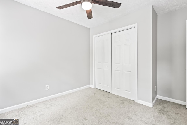 unfurnished bedroom featuring a textured ceiling, a closet, ceiling fan, and light colored carpet