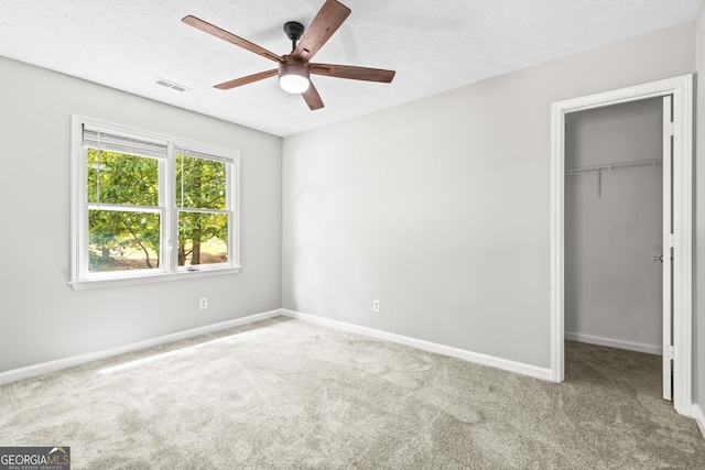 unfurnished bedroom with ceiling fan, a spacious closet, a textured ceiling, light colored carpet, and a closet