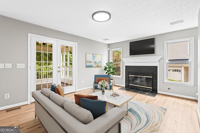 living room featuring a tile fireplace, french doors, light wood-type flooring, and plenty of natural light