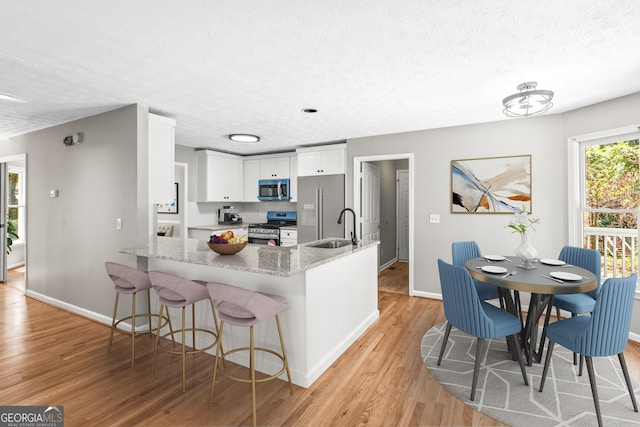 kitchen with light stone counters, light hardwood / wood-style flooring, kitchen peninsula, white cabinets, and appliances with stainless steel finishes