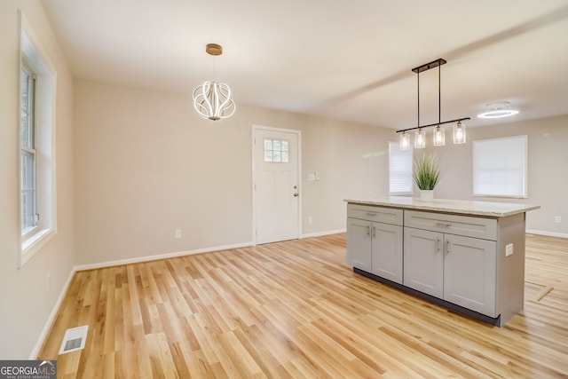 kitchen featuring light wood-type flooring, light stone counters, decorative light fixtures, an inviting chandelier, and gray cabinets