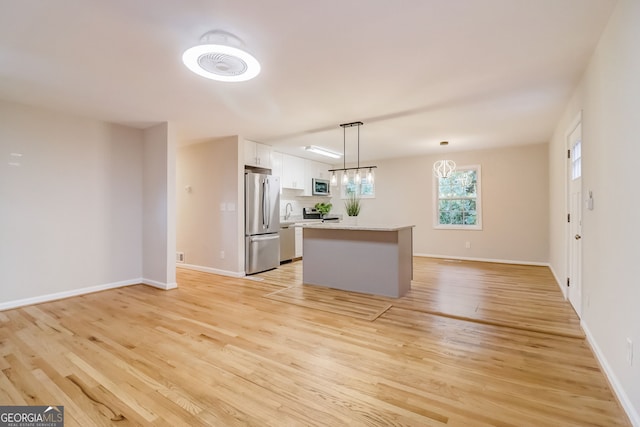 kitchen with pendant lighting, white cabinets, light wood-type flooring, appliances with stainless steel finishes, and a kitchen island