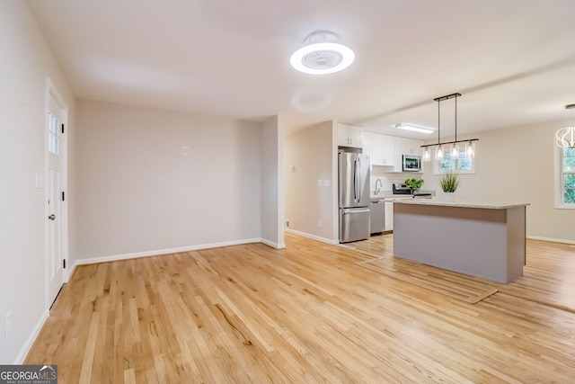 kitchen with a center island, appliances with stainless steel finishes, pendant lighting, white cabinets, and light wood-type flooring