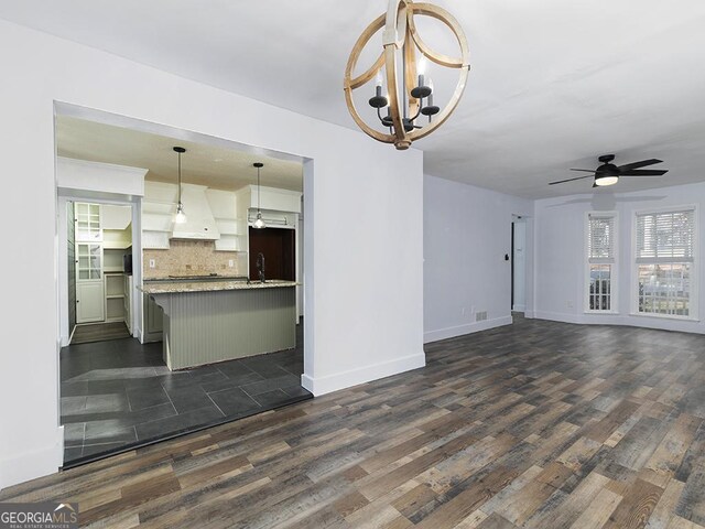 unfurnished living room featuring ceiling fan with notable chandelier and dark hardwood / wood-style flooring