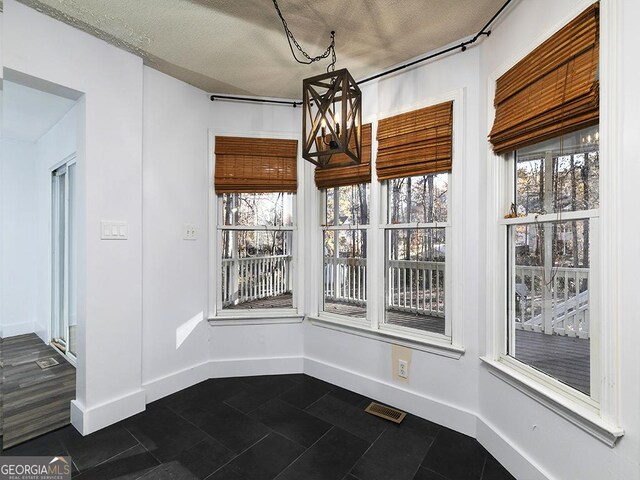 unfurnished dining area featuring dark tile patterned floors, a textured ceiling, and a notable chandelier