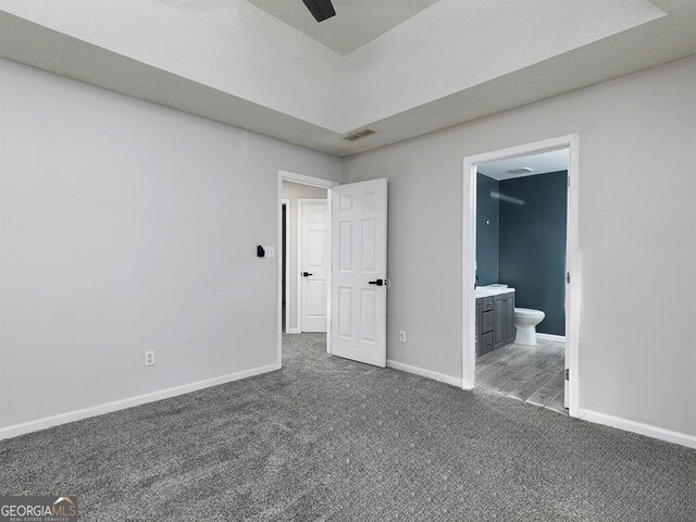 unfurnished bedroom featuring ensuite bathroom, dark carpet, and ceiling fan