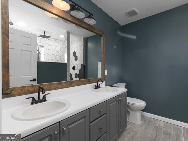 bathroom featuring a tile shower, hardwood / wood-style flooring, vanity, and toilet