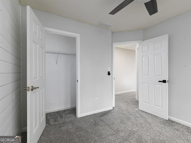 unfurnished bedroom featuring a closet, dark carpet, ceiling fan, and wood walls