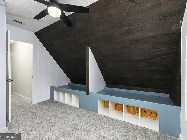 interior space featuring a textured ceiling, carpet floors, vaulted ceiling, and ceiling fan