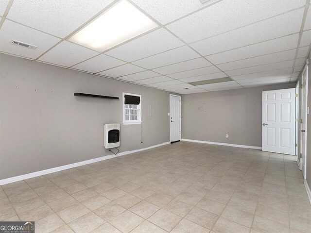 basement featuring a paneled ceiling and heating unit