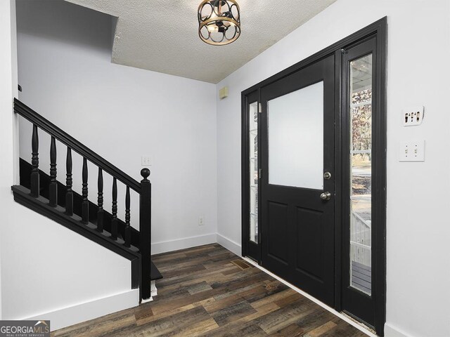 foyer entrance featuring a textured ceiling, a notable chandelier, and dark wood-type flooring