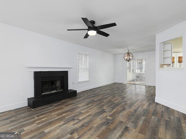 unfurnished living room with plenty of natural light, dark wood-type flooring, ceiling fan with notable chandelier, and a brick fireplace