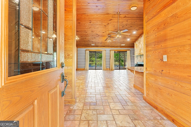 foyer entrance with wooden walls, vaulted ceiling, an outdoor stone fireplace, wood ceiling, and ceiling fan