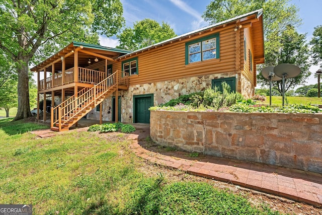 rear view of house with stairway, stone siding, a deck, log siding, and a yard