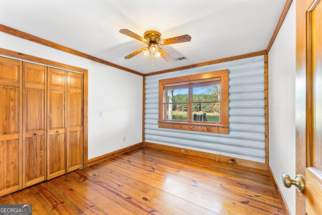 unfurnished bedroom with rustic walls, ceiling fan, ornamental molding, and hardwood / wood-style flooring