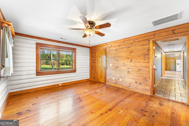 spare room with ceiling fan, wood-type flooring, and wooden walls