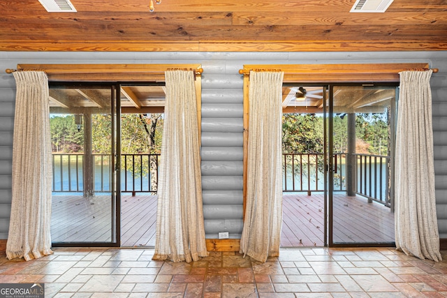 entryway with ceiling fan, a water view, and rustic walls