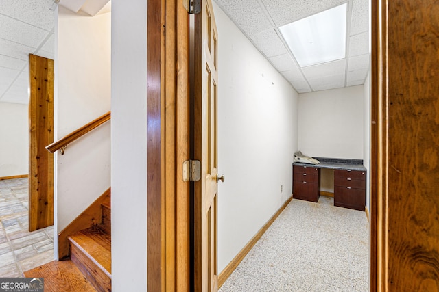 corridor with baseboards, stairs, and a drop ceiling