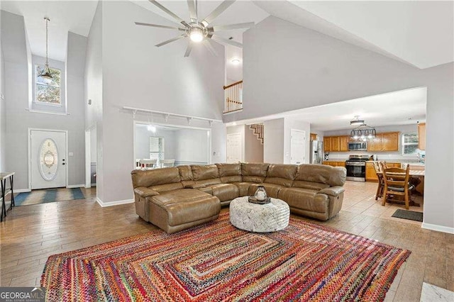 living room with high vaulted ceiling, light hardwood / wood-style floors, and ceiling fan with notable chandelier