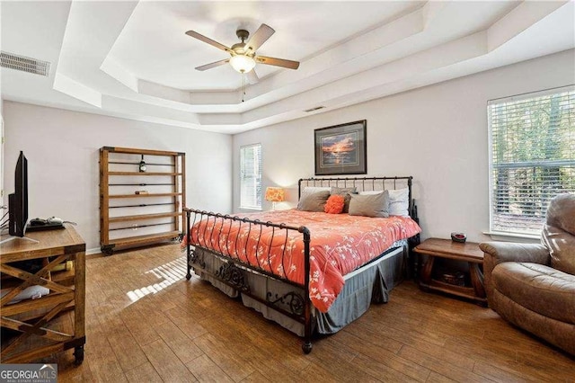 bedroom with ceiling fan, a raised ceiling, and wood-type flooring