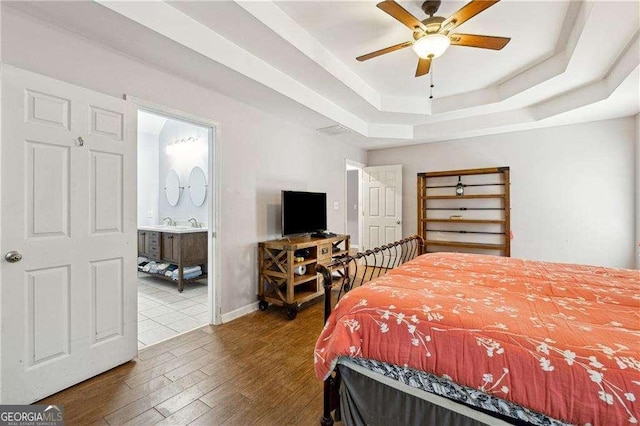 bedroom featuring dark hardwood / wood-style flooring, a tray ceiling, ceiling fan, sink, and connected bathroom