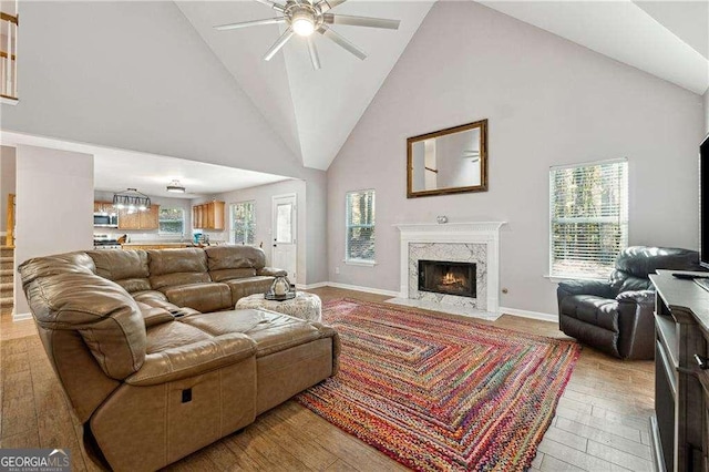 living room featuring a high end fireplace, plenty of natural light, light hardwood / wood-style floors, and high vaulted ceiling