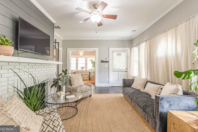 living room featuring hardwood / wood-style floors, ceiling fan, ornamental molding, and a brick fireplace