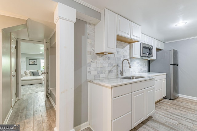 kitchen featuring appliances with stainless steel finishes, light wood-type flooring, crown molding, sink, and white cabinets