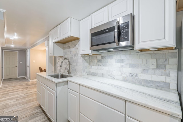 kitchen with white cabinets, sink, decorative backsplash, light stone countertops, and light hardwood / wood-style floors