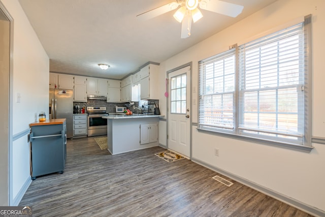 kitchen featuring kitchen peninsula, dark hardwood / wood-style floors, appliances with stainless steel finishes, tasteful backsplash, and white cabinetry