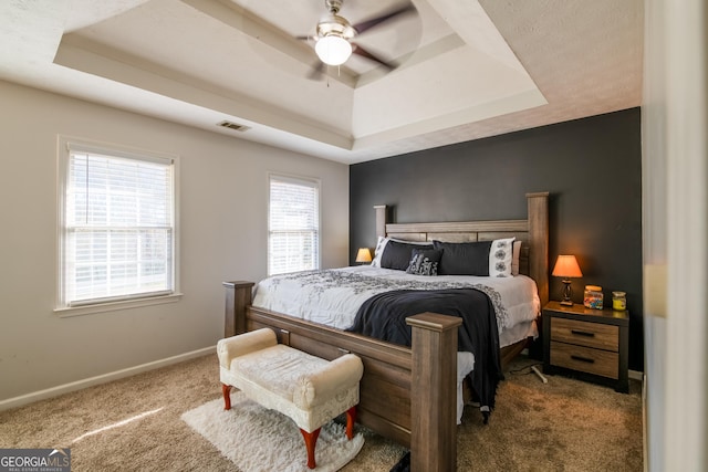 carpeted bedroom with ceiling fan and a raised ceiling