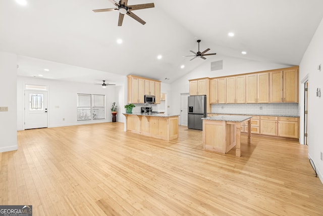 kitchen featuring decorative backsplash, a breakfast bar, appliances with stainless steel finishes, a center island with sink, and light wood-type flooring