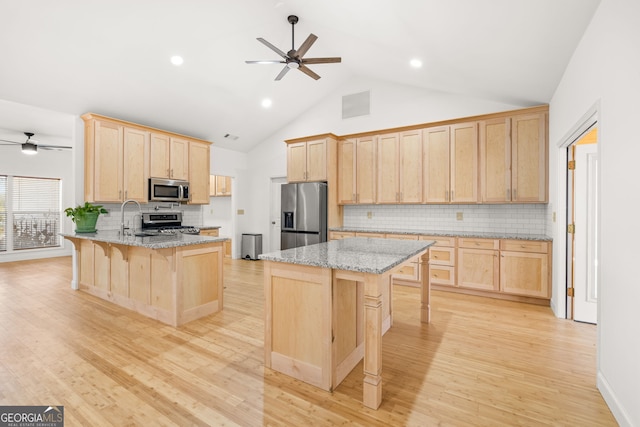 kitchen with light stone countertops, appliances with stainless steel finishes, light hardwood / wood-style flooring, and a kitchen breakfast bar